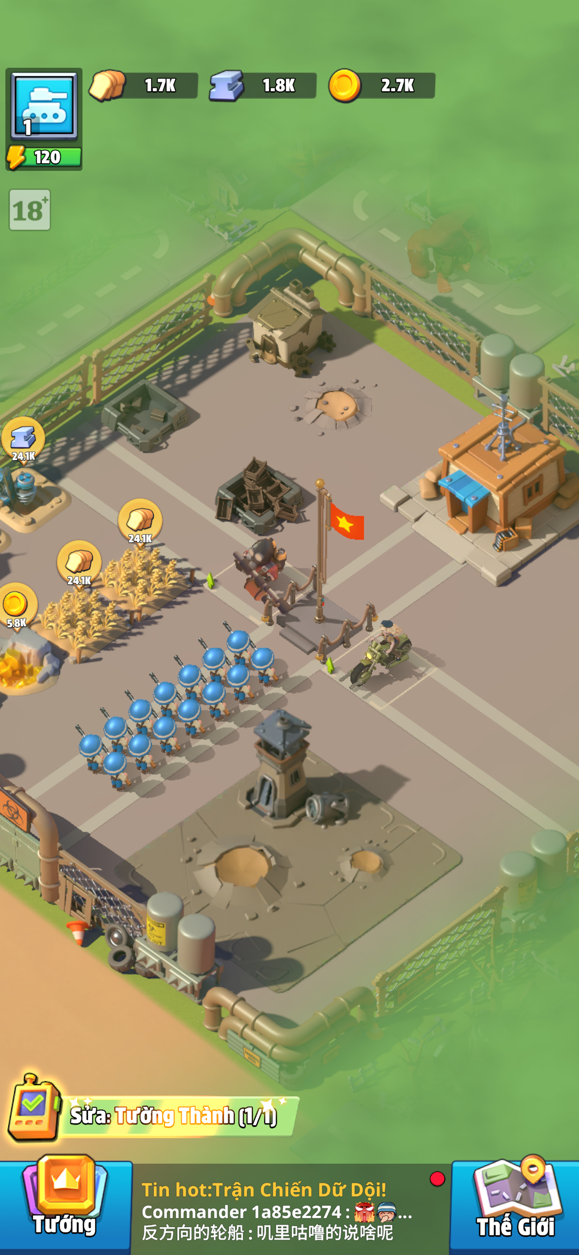 A developed base: rows of trained blue-uniformed soldiers drill on the parade ground, a Vietnamese flag marks the center, and live alliance chat scrolls at the bottom — "Tin hot: Trận Chiến Dữ Dội!" (Hot news: Fierce Battle!). The "Sức Tường Thành (1/1)" badge in the bottom bar signals a Wall repair waiting. The base is never quiet — it is teeming, and every element signals that something is always happening without you.